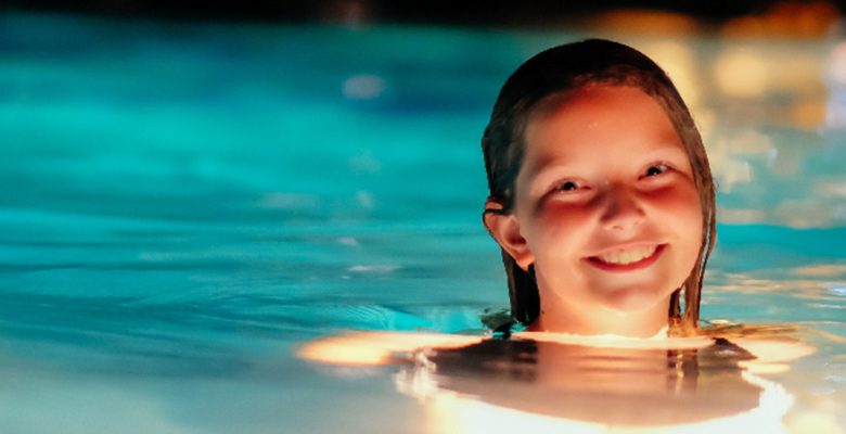 Photo of a smiling girl swimming at a night time pool party.